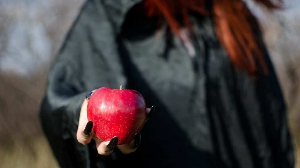 fairy tale red head holding an apple wearing a black cape