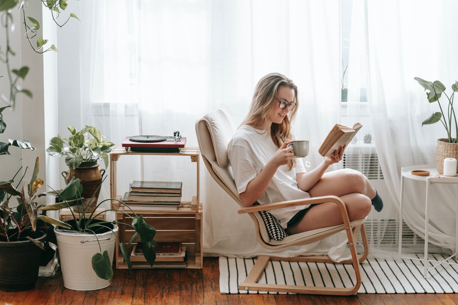 smiling woman with hot drink reading book at home